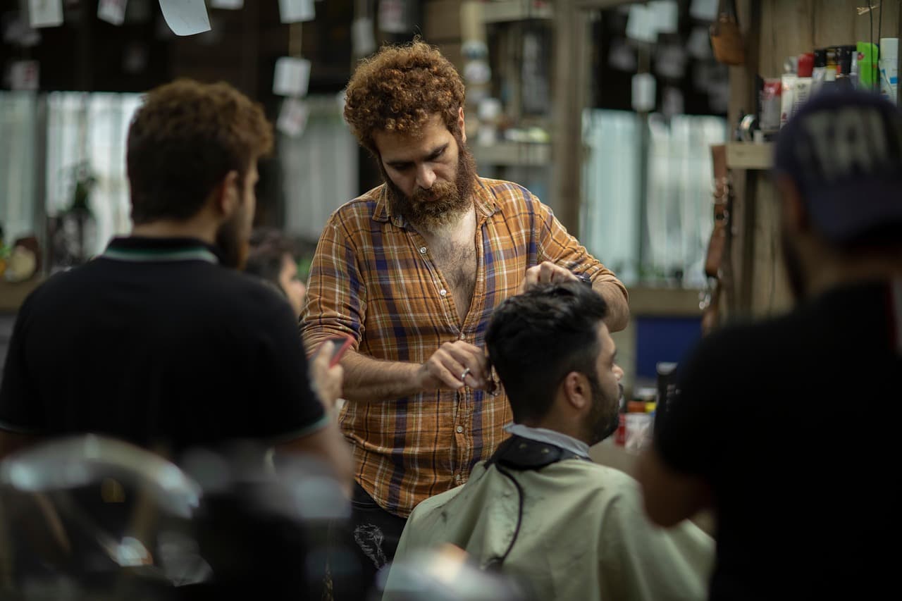 A barber working scissors through a customer’s hair in a busy shop